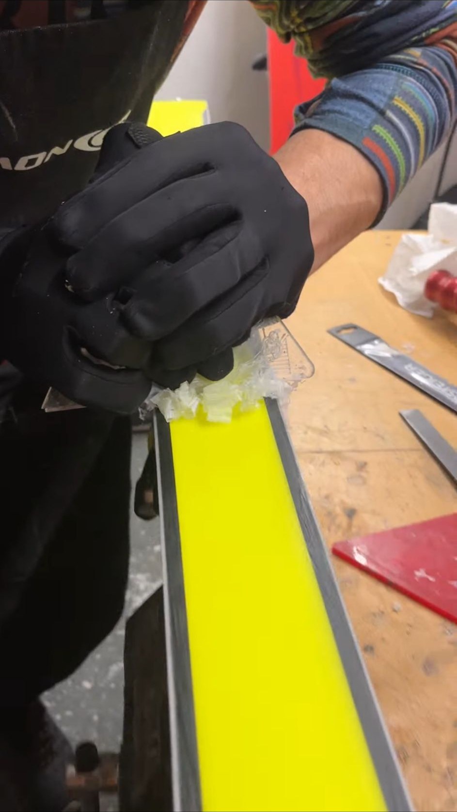 Kayak tabanına wax sürülmesi — sarı taban üzerinde mum talaşları, atölyede